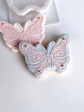 Two butterfly-shaped cookies with intricate detailing and different shades of pink and blue colors.