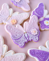 Decorative butterfly cookies with purple and white icing on a pink background
