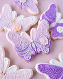 Decorative butterfly cookies with purple and white icing on a pink background