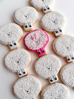 Decorative cookies shaped like sheep with white faces and black legs on a white background