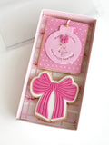 Pink cookie with a bow and matching card in a box on a white background