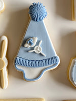 Decorative cookie shaped like a blue party hat with a white cloud and airplane on a beige background.