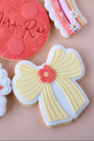 Decorative cookies with a yellow bow and red flower on a pink background