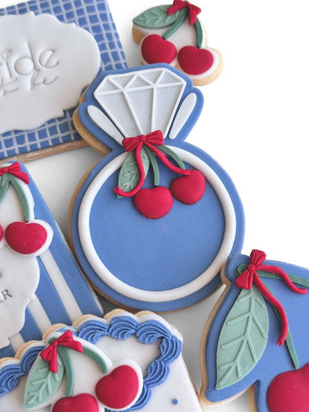Decorative cookies shaped like a diamond ring with cherries on a white surface.